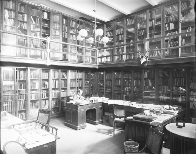 Black-and-white photograph from the 1880s of a researcher working at a desk in a library
