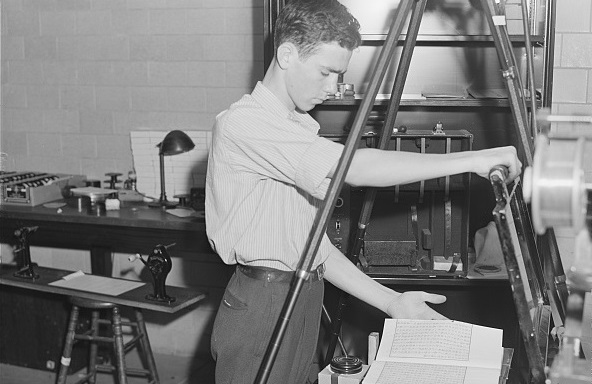 Black-and-white historical photograph of a man using a large microfilm machine
